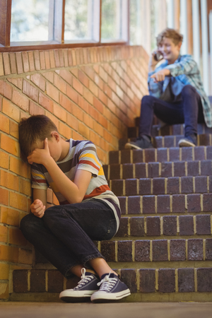 School friend bullying a sad boy in school corridor at schoolの写真素材