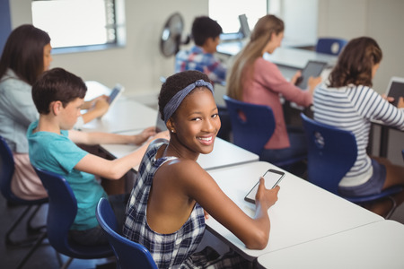 Portrait of student holding mobile phone in classroom at school
