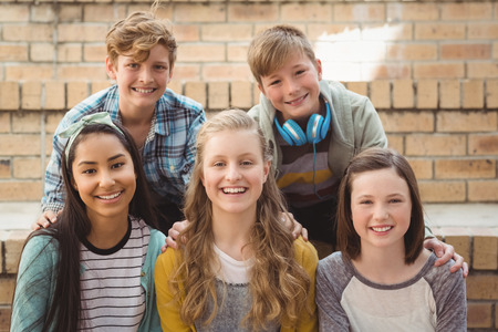Portrait of smiling school students sitting on the staircase in campus at school