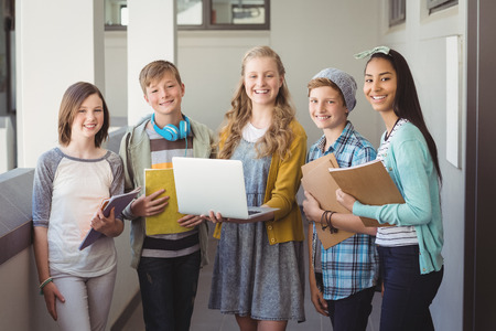 Portrait of smiling school students using laptop in corridor at schoolの写真素材