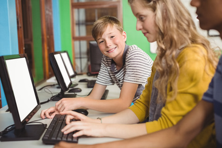 Smiling students studying in computer classroom at schoolの写真素材