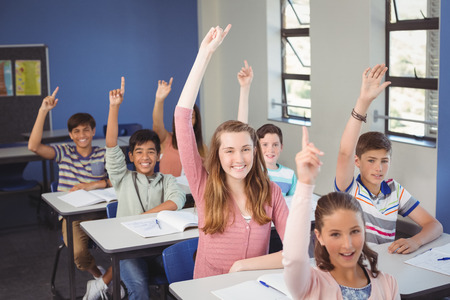Portrait of school kids raising hand in classroom at schoolの写真素材