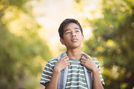 Smiling schoolboy standing with schoolbag in campus at schoolの写真素材