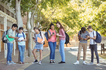 Students using mobile phone on road in campus at schoolの写真素材