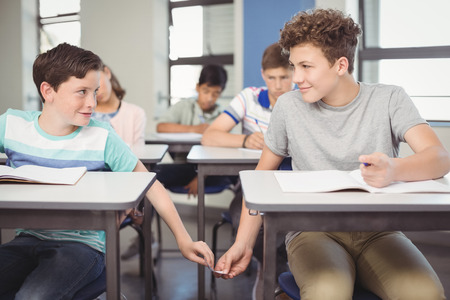 School students passing a chit in a secretive way inside the classroom at school