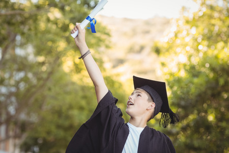 Excited graduate schoolboy with degree scroll in campus at school