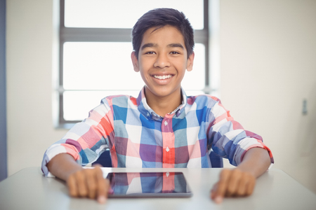 Portrait of schoolboy with digital tablet at desk in classroomの写真素材