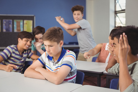 School friends bullying a sad boy in classroom at schoolの写真素材
