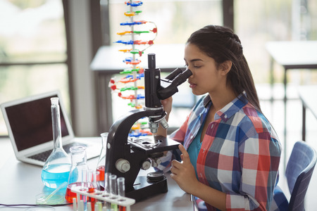 Attentive schoolgirl looking through microscope in laboratory at schoolの写真素材