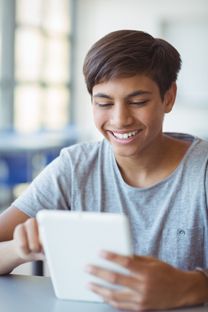 Happy schoolboy using digital tablet in classroom at schoolの写真素材