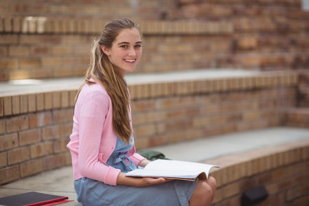 Portrait of schoolgirl reading book in campus at schoolの写真素材