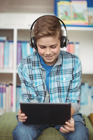 Happy schoolboy listening music while using digital tablet in library at schoolの写真素材