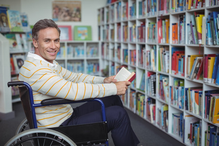 Portrait of disabled school teacher holding book in library at schoolの写真素材
