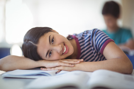 Portrait of happy schoolgirl leaning on bench in classroom at school