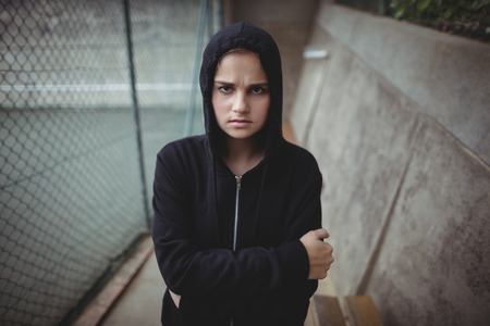 Portrait of anxious teenage girl standing with arms crossed at school campus