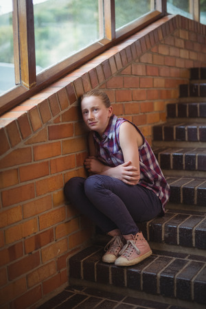 Sad schoolgirl sitting alone on staircase in schoolの写真素材