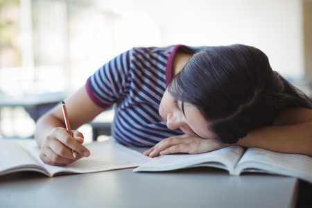 Tired schoolgirl sleeping in classroom at schoolの写真素材