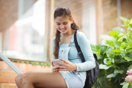 Happy schoolgirl using mobile phone in schoolの写真素材