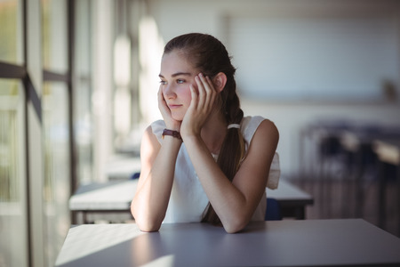 Thoughtful schoolgirl sitting in classroom at schoolの写真素材