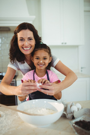 Portrait of mother and daughter breaking egg in bowl while preparing cookie in kitchenの写真素材