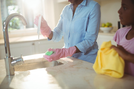Mother assisting her daughter in cleaning utensils at home