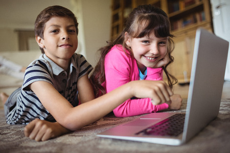 Portrait of siblings using laptop in living room at homeの写真素材
