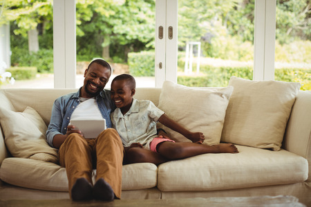 Father and son using digital tablet in living room at homeの写真素材