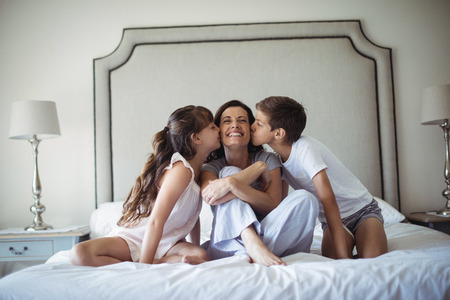 Kids kissing their mother on cheek in bedroom at homeの写真素材
