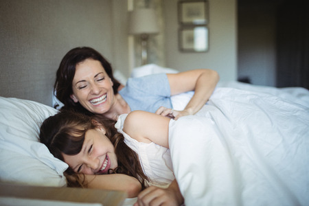 Mother and daughter laughing in bed at homeの写真素材