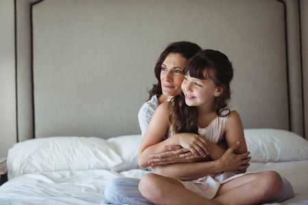 Portrait of mother embracing her daughter in bedroom at homeの写真素材