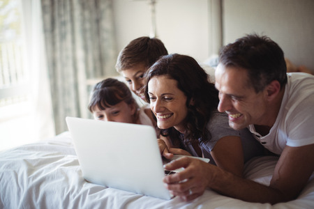 Happy family using laptop on bed in bedroom at homeの写真素材