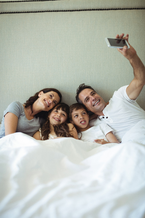 Parents and kids taking a selfie on bed at homeの写真素材