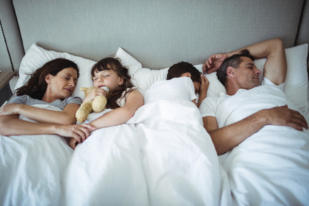 Parents and kids sleeping on bed at homeの写真素材