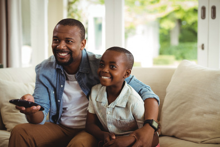 Son and father watching television at homeの写真素材