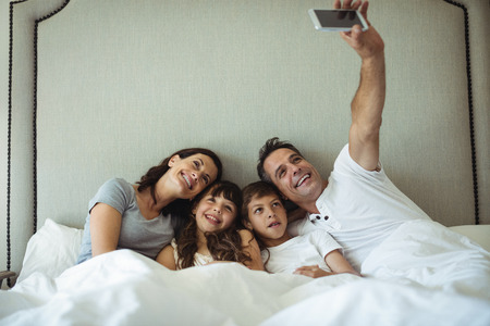 Parents and kids taking a selfie on bed at homeの写真素材