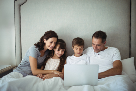 Parents and kids using laptop in bed at homeの写真素材