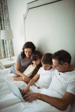 Parents and kids using laptop in bed at homeの写真素材
