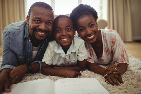 Portrait of parents and son reading a book while lying on a rug at homeの写真素材