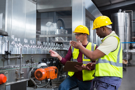 Two factory workers discussing while monitoring drinks production line at factoryの写真素材