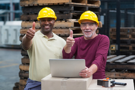 Portrait of two factory workers with laptop showing their thumbs up in drinks production plantの写真素材