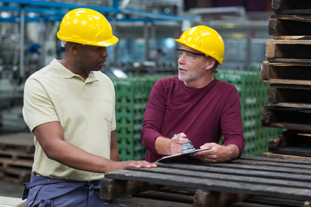 Two factory workers discussing with a clipboard in drinks production plant