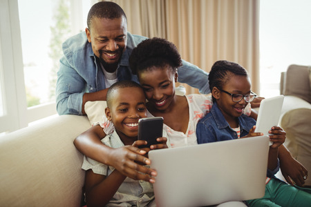 Parents and kids using laptop, smartphone and digital tablet on sofa at homeの写真素材