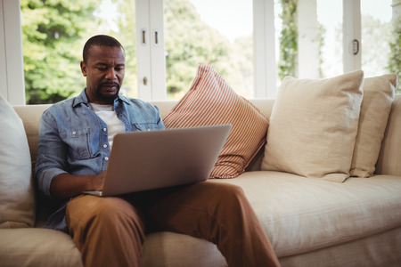 Man sitting on sofa and using laptop in living room at homeの写真素材
