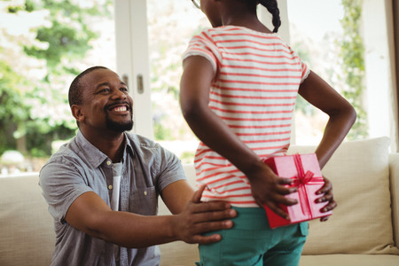 Daughter hiding gift behind her back for father at homeの写真素材