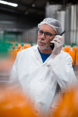 Factory engineer talking on walkie talkie in bottle factoryの写真素材