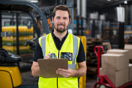 Smiling factory worker writing on clipboard in factoryの写真素材