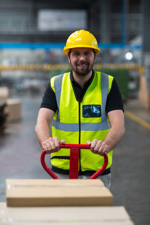 Portrait of smiling factory worker pulling trolley of cardboard boxes in factoryの写真素材