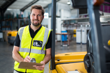 Smiling factory worker writing on clipboard in factoryの写真素材
