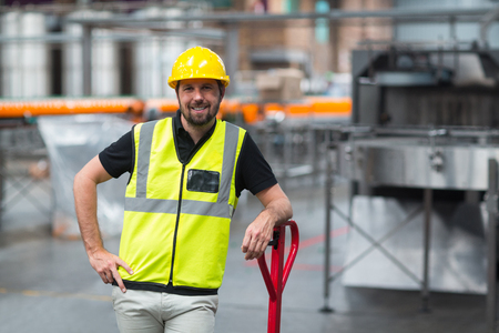 Portrait of smiling factory worker standing with hand on hip in factoryの写真素材