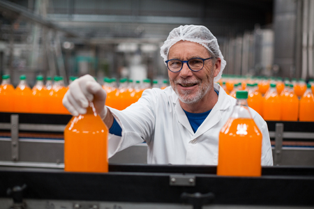 Portrait of smiling factory engineer examining a bottle of juice in bottle factoryの写真素材